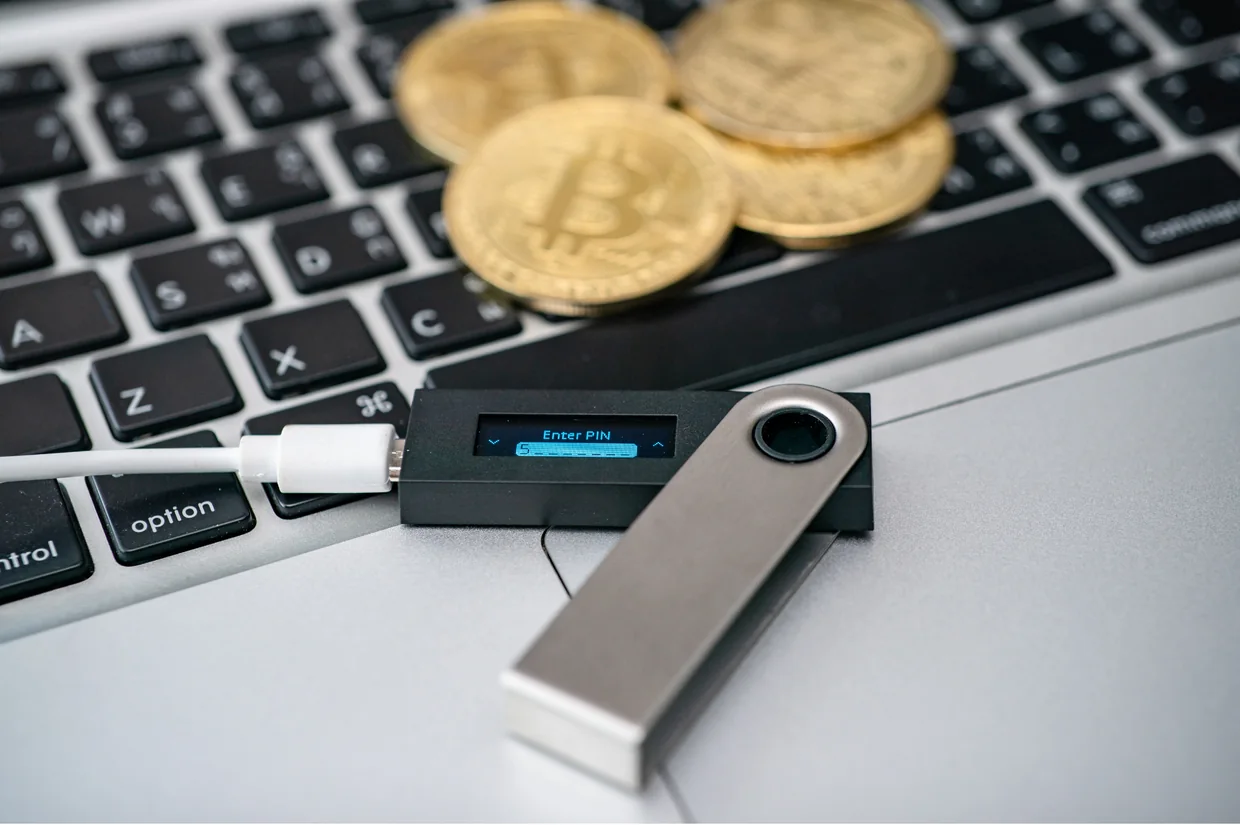 Hardware Wallet mit PIN-Abfrage auf einer Laptoptastatur, daneben goldene Bitcoin-Münzen