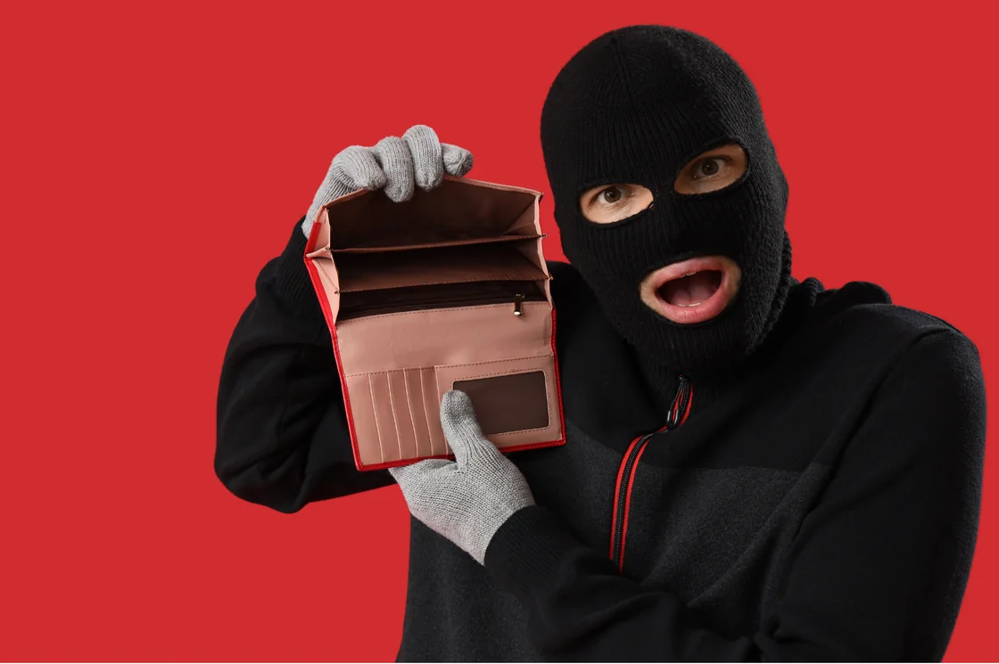 Maskierte Person hält eine geöffnete, leere Geldbörse in die Kamera