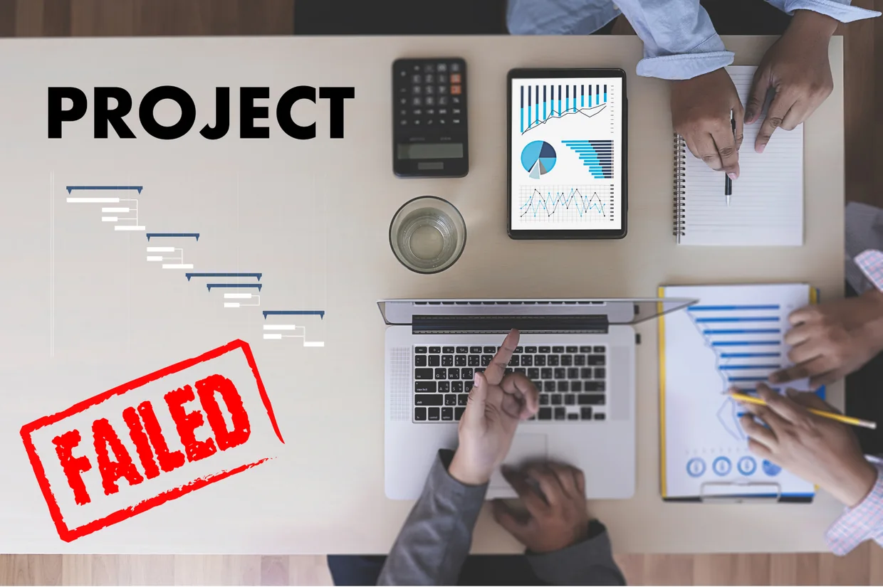 Schreibtisch von oben mit Laptop, Tablet und Diagrammen, darüber ein roter Stempel mit der Aufschrift Project Failed