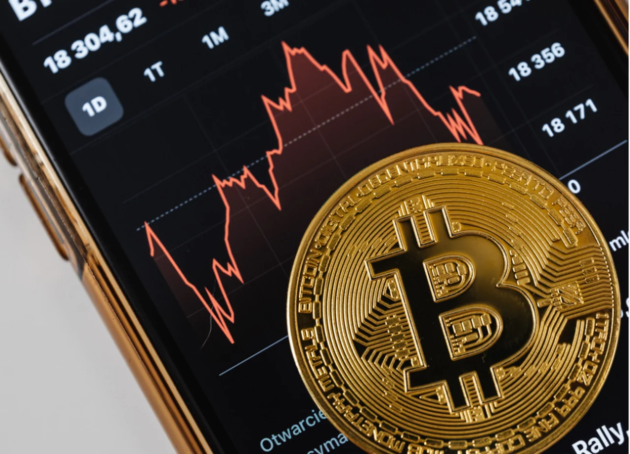 Bitcoin-Münze auf einem Smartphone, das einen fallenden Kursverlauf zeigt